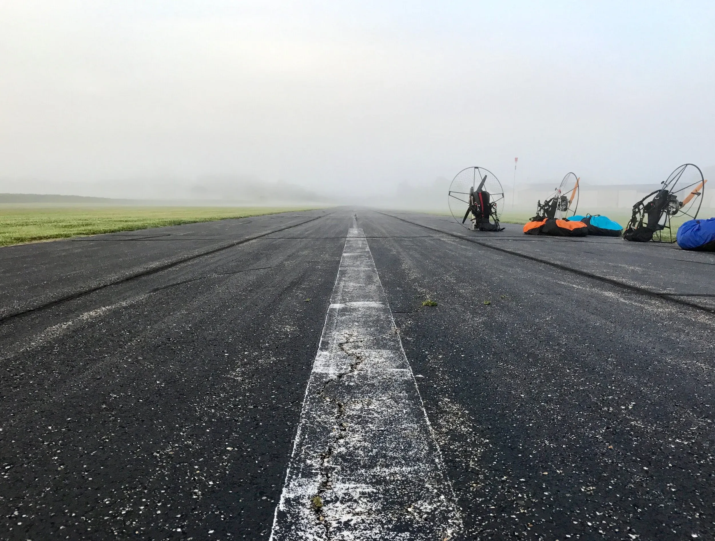 Paramotors sitting on an airport runway, waiting for fog to clear